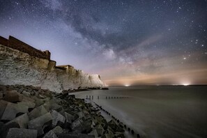 Un paisaje costero con cielo estrellado, un acantilado y un mar tranquilo.