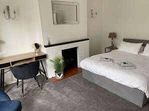 Una habitación de hotel con cama, escritorio, sillón, chimenea y mesita de noche con lámpara.