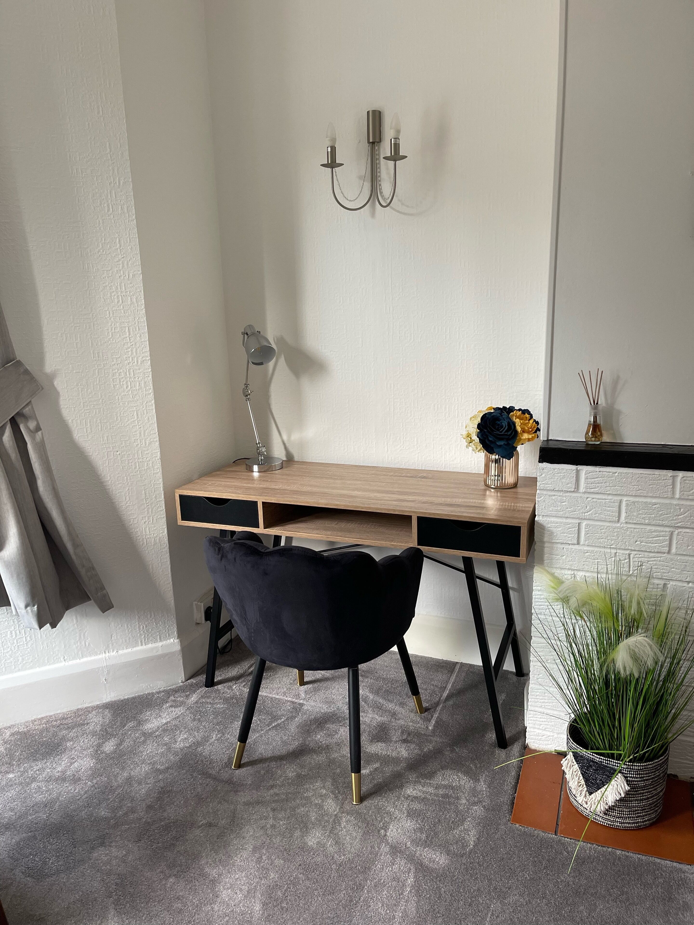 Un espacio de trabajo con escritorio, silla, lámpara, aplique y una planta en maceta.