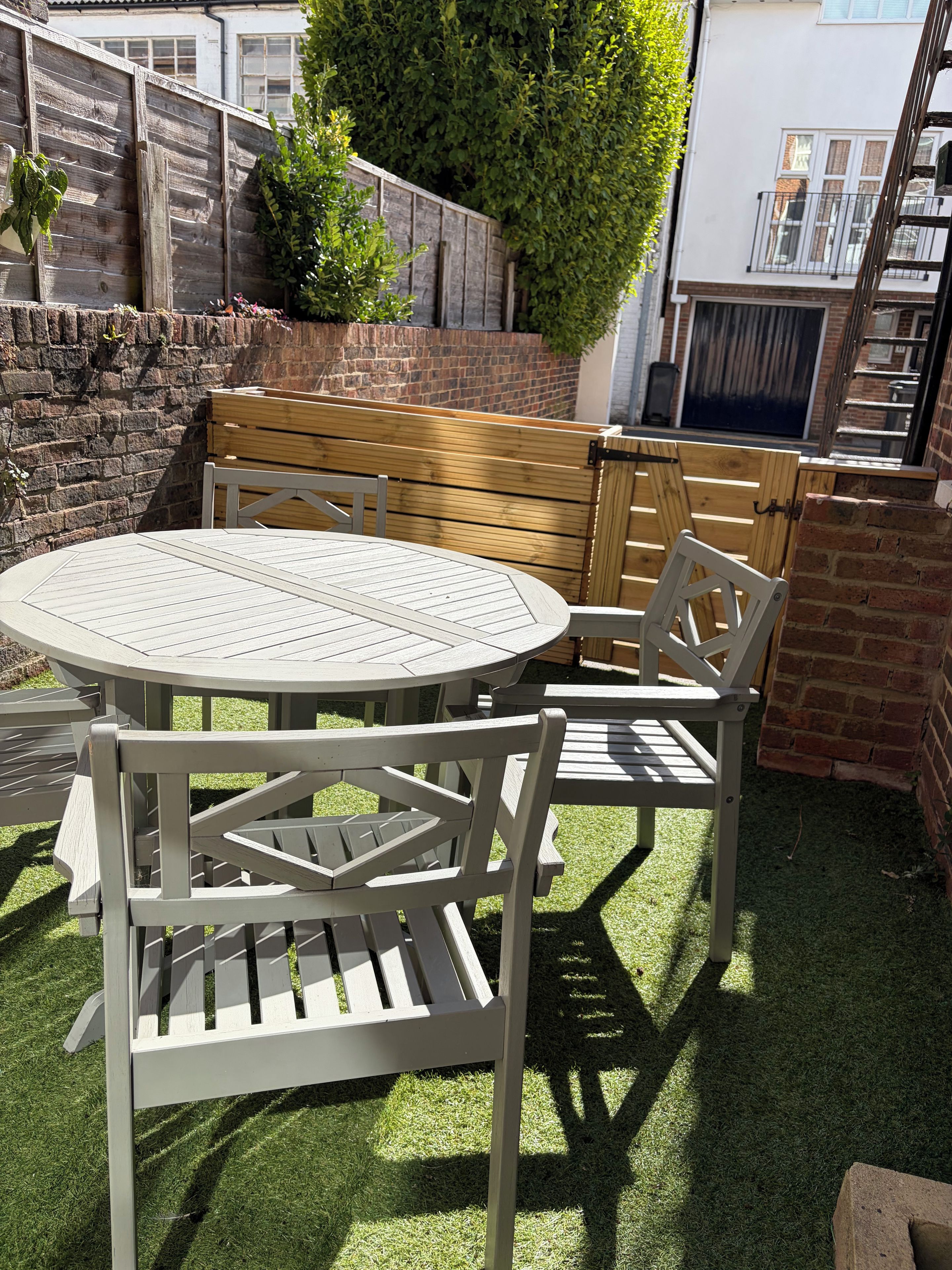 Un patio con una mesa redonda y cuatro sillas, rodeado por un muro de ladrillo y una cerca de madera.