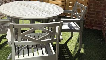 Un patio con una mesa redonda y cuatro sillas, rodeado por un muro de ladrillo y una cerca de madera.