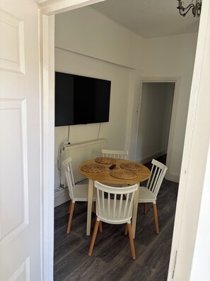 Comedor con una mesa redonda, cuatro sillas, un televisor de pantalla plana en la pared y un radiador debajo.