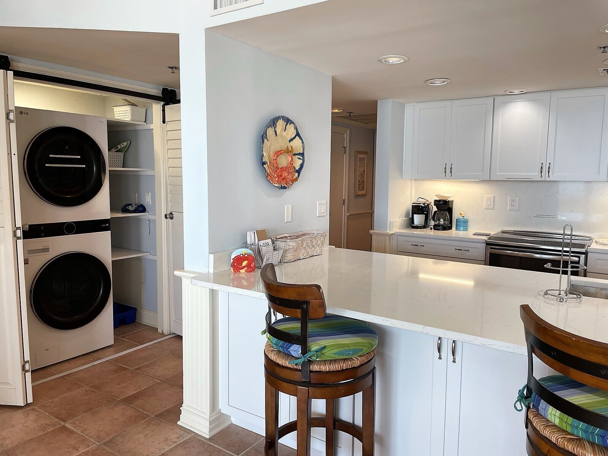 Cocina con isla central, muebles blancos y lavadora en el área de lavandería contigua.