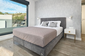 A bedroom with a large bed, bedside lamps, a nightstand, and a view through a window.