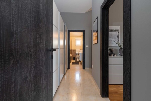 A hallway with a dark wooden door, a tiled floor, and a view into a bathroom with a toilet and a small window. - Apartment 8 with a stunning view (Trogir)