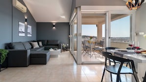 En moderne stue med en grå sofa, et spiseområde med bord og stole, samt en balkon med udsigt.