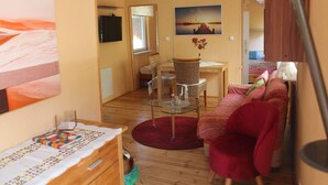 En hyggelig stue med en rød sofa, et glasbord og et spiseområde med fletstole.