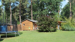En træhytte med hegnede gård, trampolin og et lille skur.