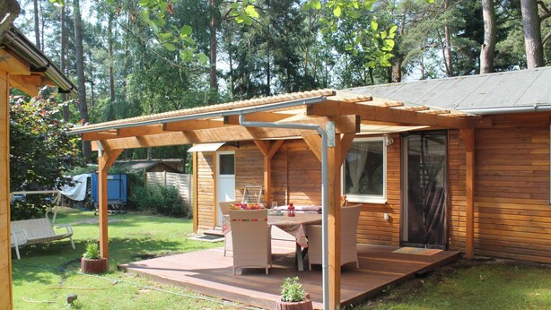 En træhytte med terrasse, spisebord og overdækket udendørs siddeplads.