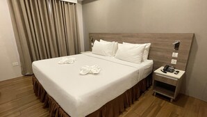 A hotel room with a large bed, a bedside table with a phone and remote, and a curtain. - Rogen Inn (Davao)