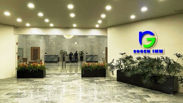 A hotel lobby with a reception desk, a large logo, and potted plants. - Rogen Inn (Davao)