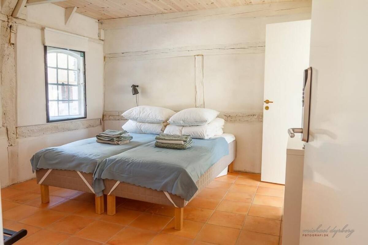 Quarto com cama, almofadas e janela.