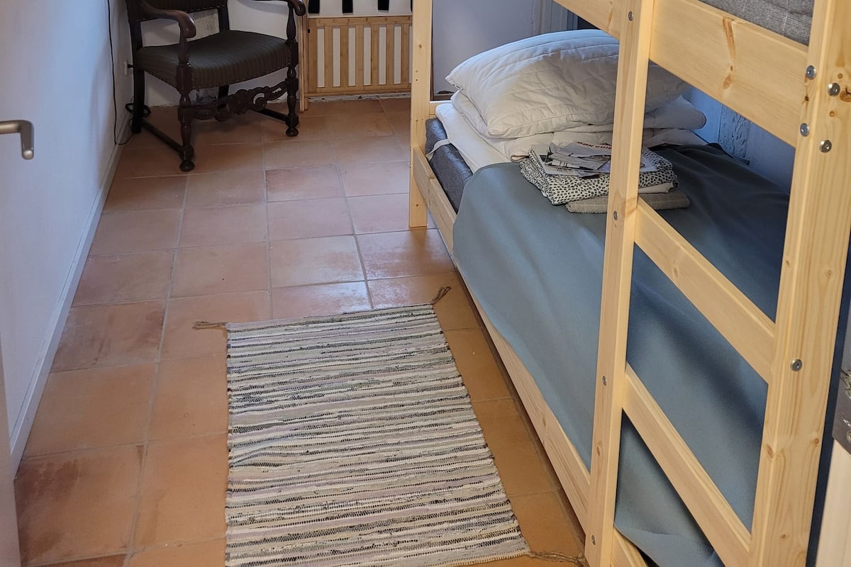 Um quarto com beliche, uma cadeira, uma escrivaninha e uma janela.