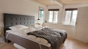 Un dormitorio con cama, piso de madera, paredes blancas y una ventana con vistas.