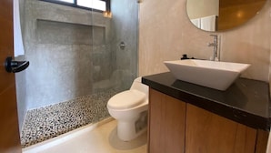 Un baño moderno con inodoro independiente, lavamanos sobre encimera y zona de ducha con puerta de cristal.