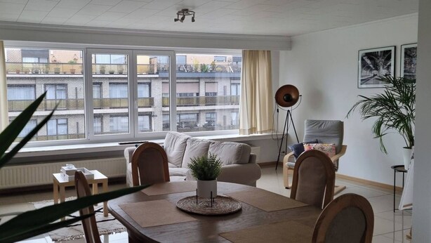 A modern living room with a large window, a dining table, and a sofa. - Superb Appartment in Antwerpen (Antwerp)