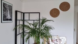 A room with a large potted plant, two framed black-and-white photographs, and two woven wall decorations. - Superb Appartment in Antwerpen (Antwerp)
