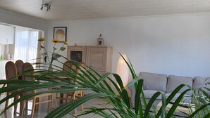 A living room with a sofa, a dining table with chairs, a kitchen area, and a large plant. - Superb Appartment in Antwerpen (Antwerp)