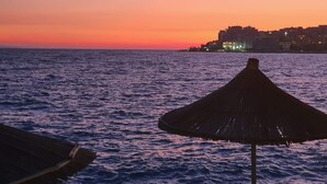 A sunset over the sea with a building in the background. - Olea Residence, Luxury sea View Apartment With Private Beach (Himarë)