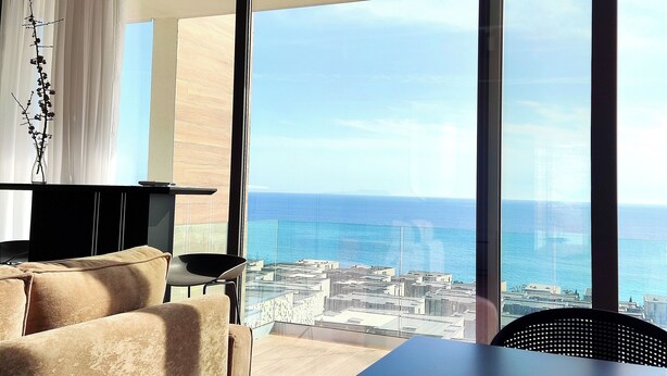 A modern room with a large window, a sofa, a small table, and a decorative vase. - Olea Residence, Luxury sea View Apartment With Private Beach (Himarë)