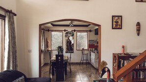 Amplia sala de estar con un sofá oscuro, una escalera de madera y un comedor con mesa y sillas.