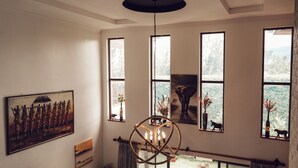 Una habitación con ventanas amplias, una pintura, una escultura y una araña.
