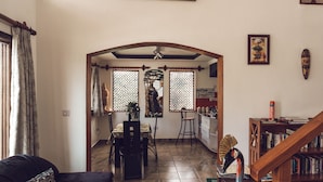 A spacious living area with a dark-colored sofa, a wooden staircase, and a dining area with a table and chairs. - Room-kilihouse B&b Large Ensuite Double (Kilimambogo)