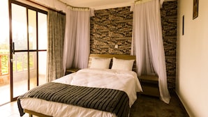 A bedroom with a large bed, a stone wall, and a balcony with curtains. - Room-kilihouse B&b Large Ensuite Double (Kilimambogo)