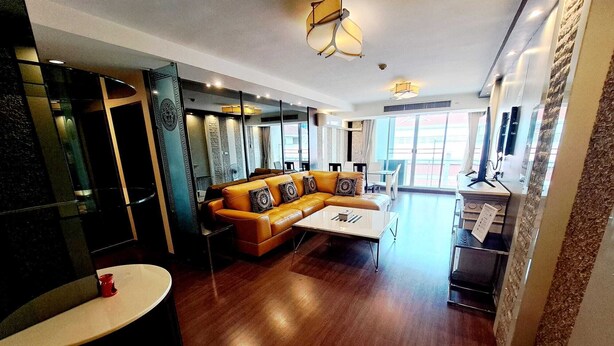 Una sala de estar moderna con un sofá de cuero, una mesa de centro y un televisor. Hay ventanas amplias y vistas al exterior.