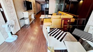 Una sala moderna con un sofá, una mesa de centro y un televisor. Hay un ventilador en el suelo y una escalera que sube a otro nivel.