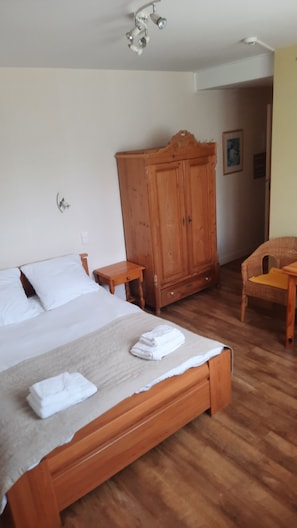 A bedroom with a wooden bed, a wooden wardrobe, a small wooden table, and a wicker chair.