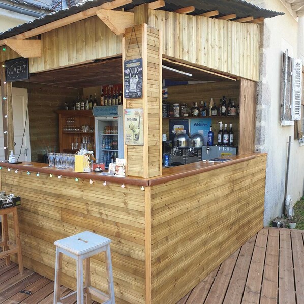 A wooden bar with a refrigerator stocked with beverages, a cash register, and a variety of liquor bottles.