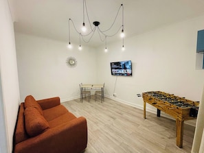 Un salon avec un canapé, une table, un téléviseur et un baby-foot.