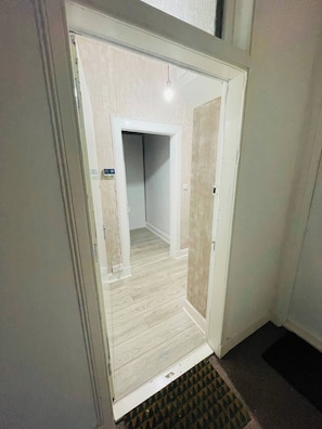 Un pasillo con una puerta que da a una habitación, una lámpara arriba y un felpudo estampado en la entrada.