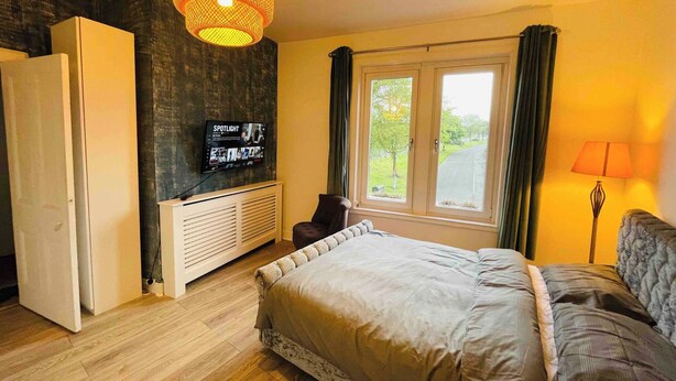 A bedroom with a bed, a television mounted on the wall, a radiator, and a window with curtains. - 1 Bedroom Pet Friendly Apt Wd Free Wifi, Parking, Netflix & Pool Table. Sleeps 3 (Kelty)