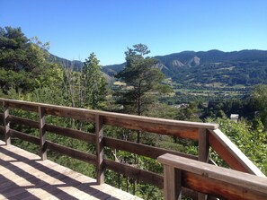 Um deck de madeira com guarda-corpo, de frente para uma paisagem montanhosa.