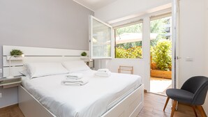 A modern bedroom with a large bed, a bedside table with a lamp, and a view of the garden through an open door. - Amazing Viale Trastevere with Terrace (Roma)