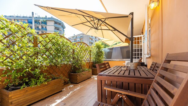 A wooden deck with a table and chairs, surrounded by planters with greenery. - Amazing Viale Trastevere with Terrace (Roma)