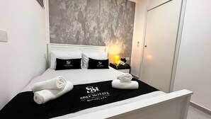 Ein Hotelzimmer mit einem Bett, zwei schwarzen Kissen mit dem Hotel-Logo, einem Nachttisch mit einer Lampe und Handtüchern auf dem Bett.