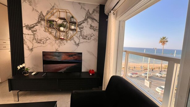 Ein modernes Wohnzimmer mit einem großen Fernseher, einem dekorativen sechseckigen Regal und Blick auf den Strand.