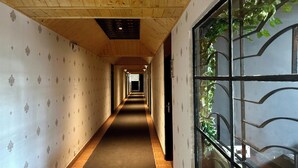 Um corredor comprido e estreito com papel de parede estampado, teto de madeira e uma janela com grade de metal.