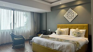 Quarto de hotel moderno com cama grande, uma cadeira, uma mesinha e um detalhe decorativo na parede.