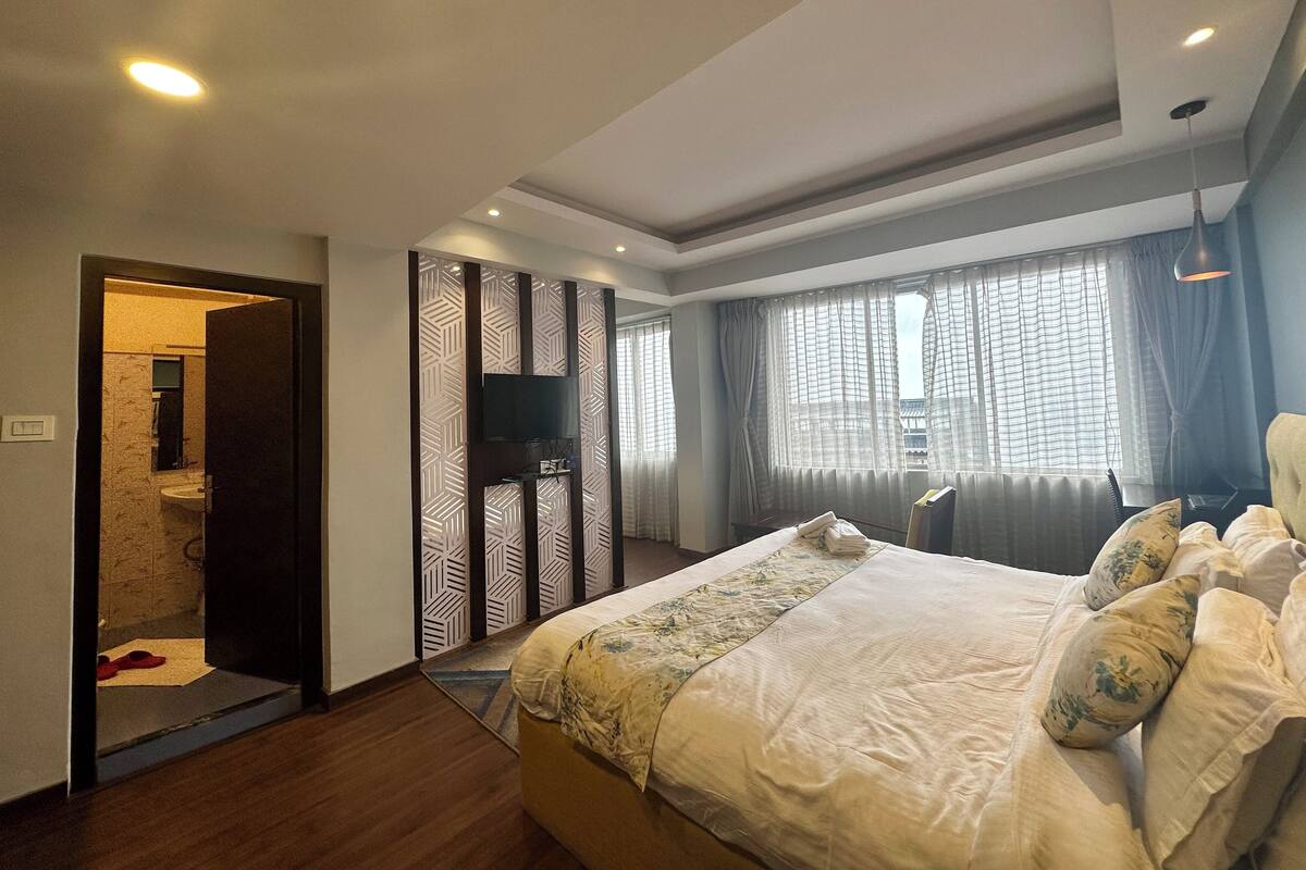 Ein Schlafzimmer mit einem Bett, einem Fernseher, einem Schreibtisch und einem Fenster mit Vorhängen.