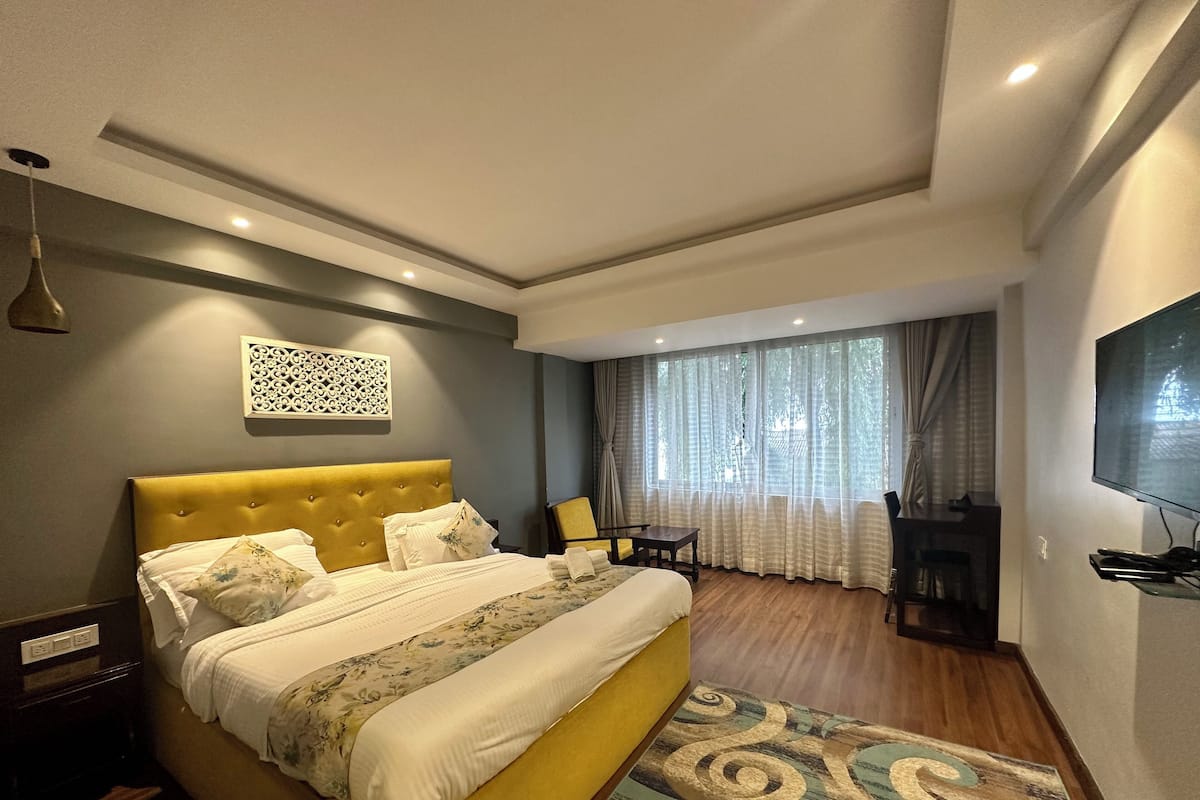 Ein Hotelzimmer mit einem großen Bett, einem Fernseher, einem Schreibtisch und einem Fenster mit Vorhängen.