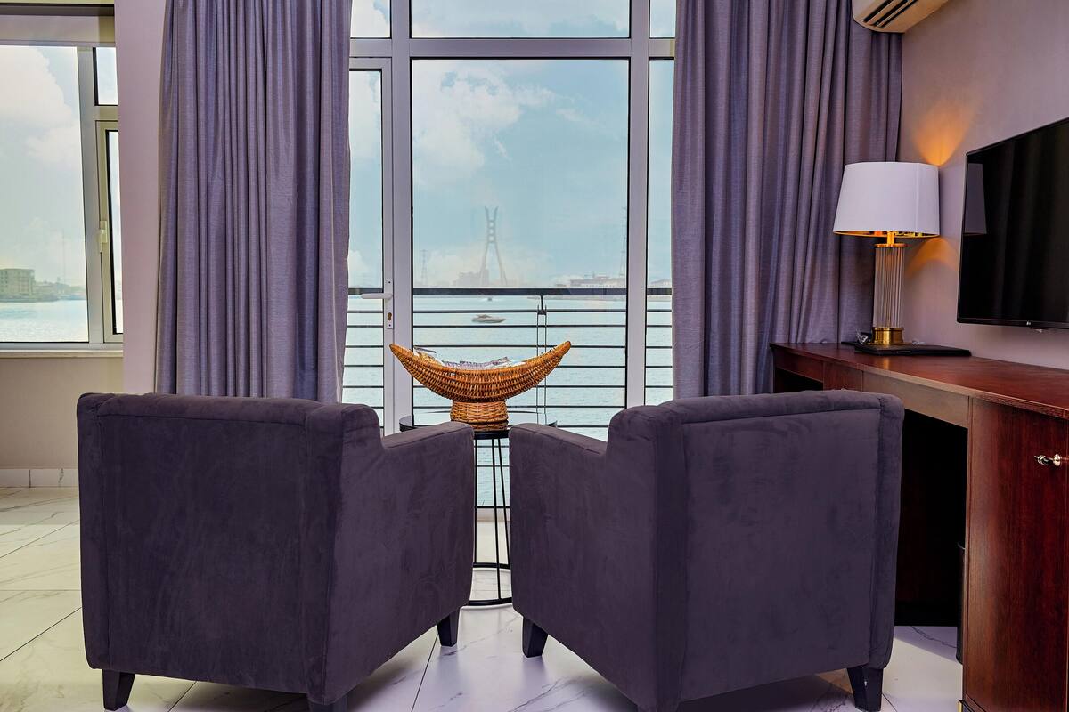 A room with two dark sofas, a wicker chair, a TV, and a view of a bridge over water.