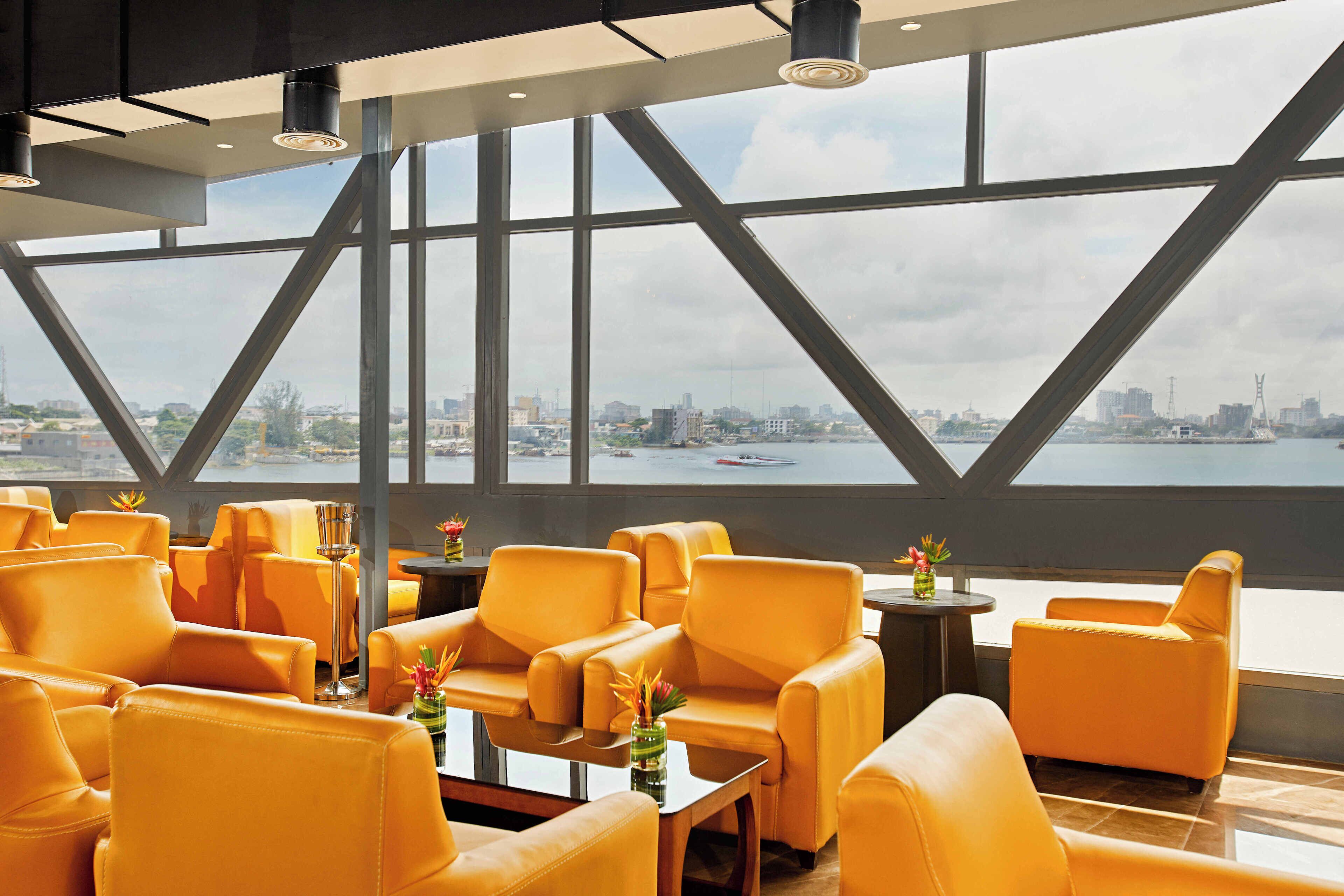A modern interior with orange leather chairs and tables, large windows offering a city view.