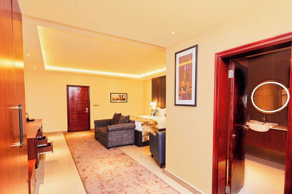 A hotel room with a sofa, a bed, a desk, and a bathroom with a sink and mirror.