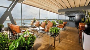 A modern lounge with leather chairs, tables, and potted plants, overlooking a body of water. - The Yacht Hotel (Lekki)