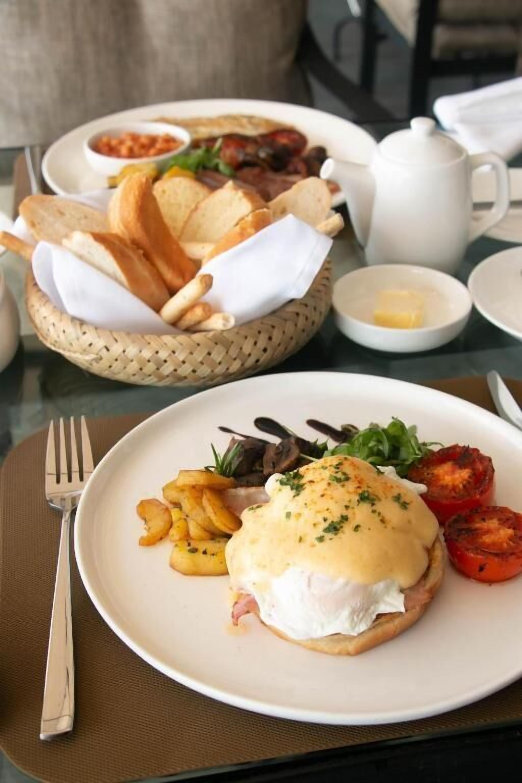 A breakfast setting with a plate of eggs benedict, toast, and tomatoes.