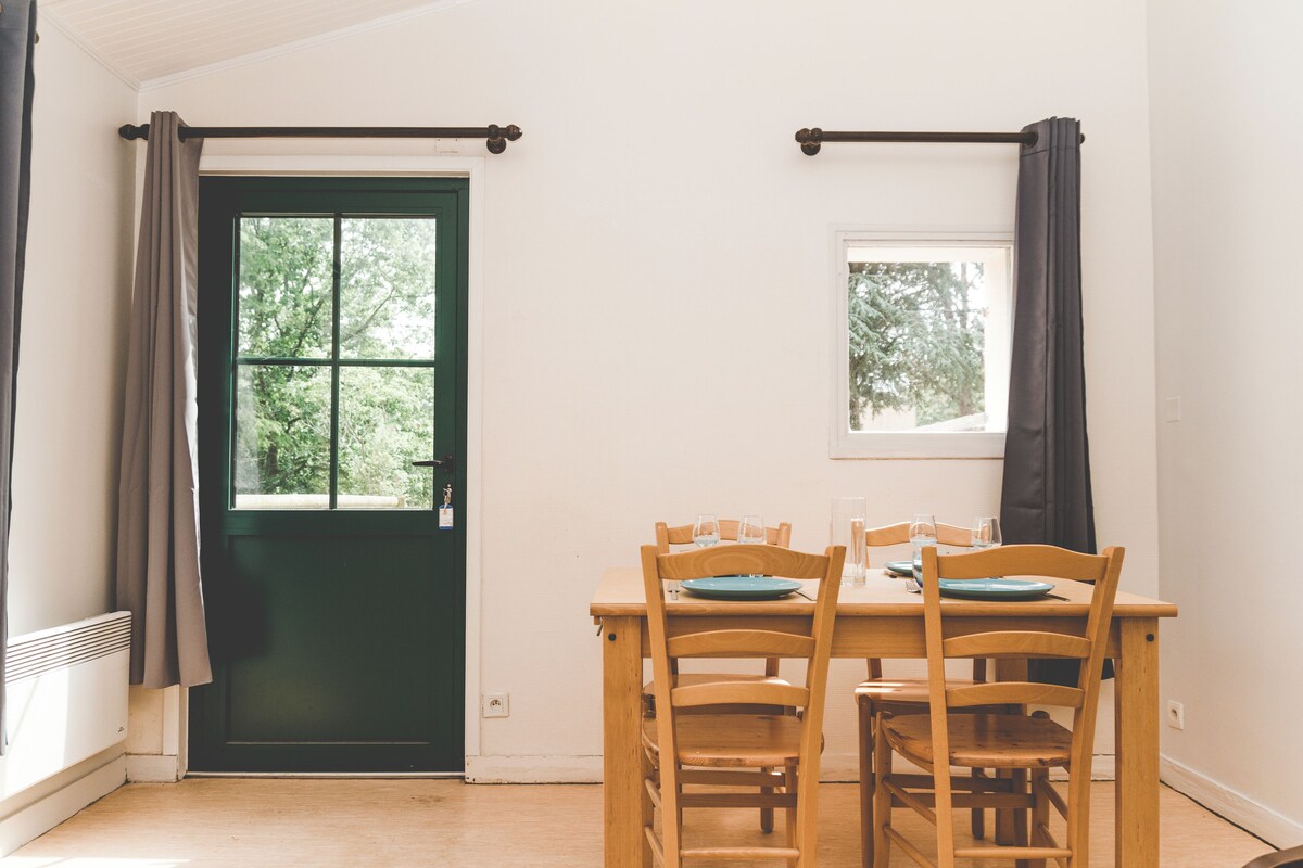 A dining area with a table set for four, a window with curtains, and a door with a view of greenery outside.